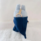 Back view of a  Labubu doll wearing a dark navy cape.
