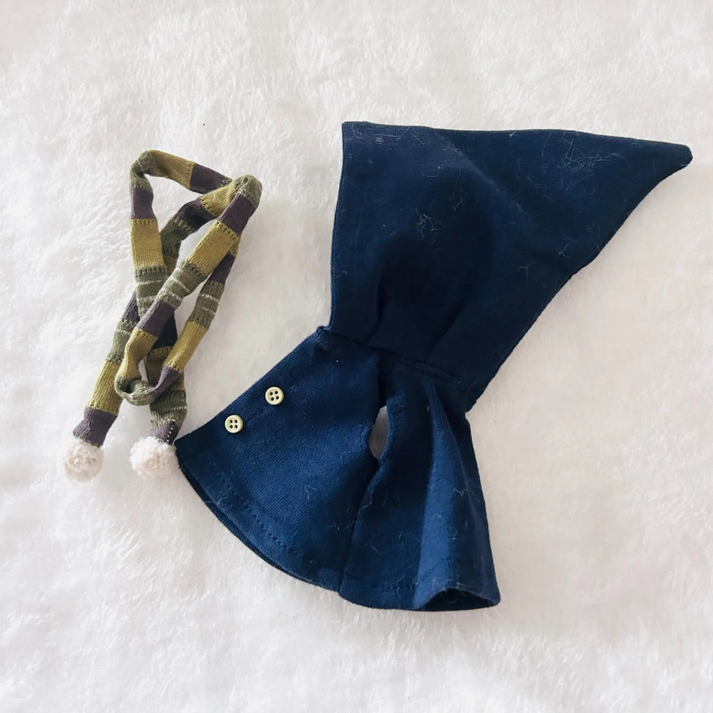 A navy blue cape with two small buttons and a matching olive green and black plaid ribbon tie with white pom-poms.