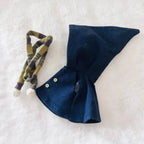 A navy blue cape with two small buttons and a matching olive green and black plaid ribbon tie with white pom-poms.