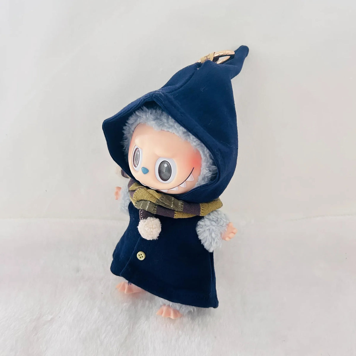 A Labubu plush doll wearing a dark navy blue pointed hooded coat with a plaid scarf.