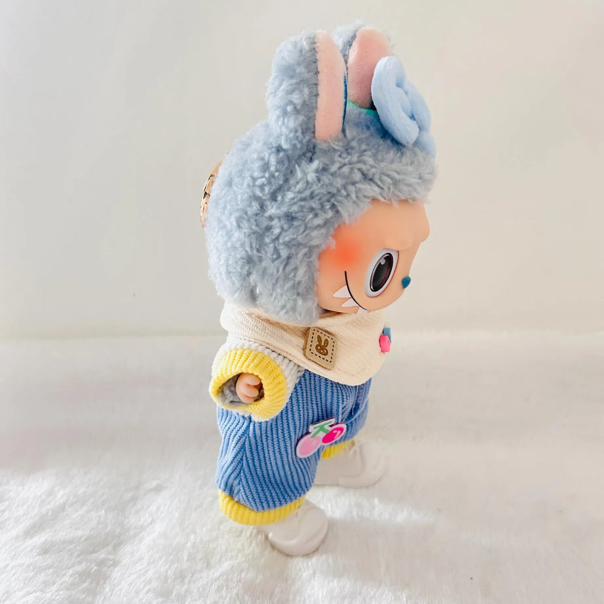 A Labubu doll wearing a blue bow, blue corduroy jumpsuit, and white shoes.