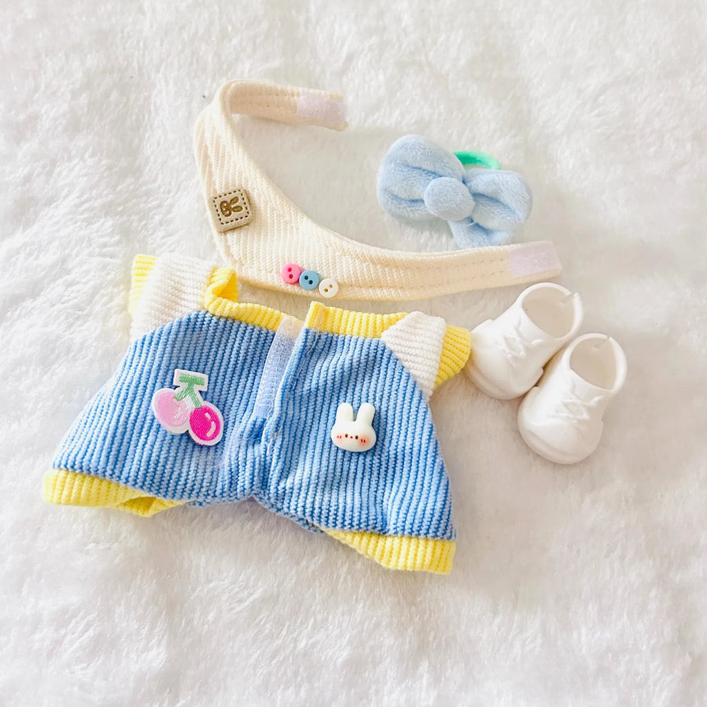 A top view of a doll outfit set, including a blue-and-yellow striped romper with yellow trim, a light blue bow headband, and small white booties.