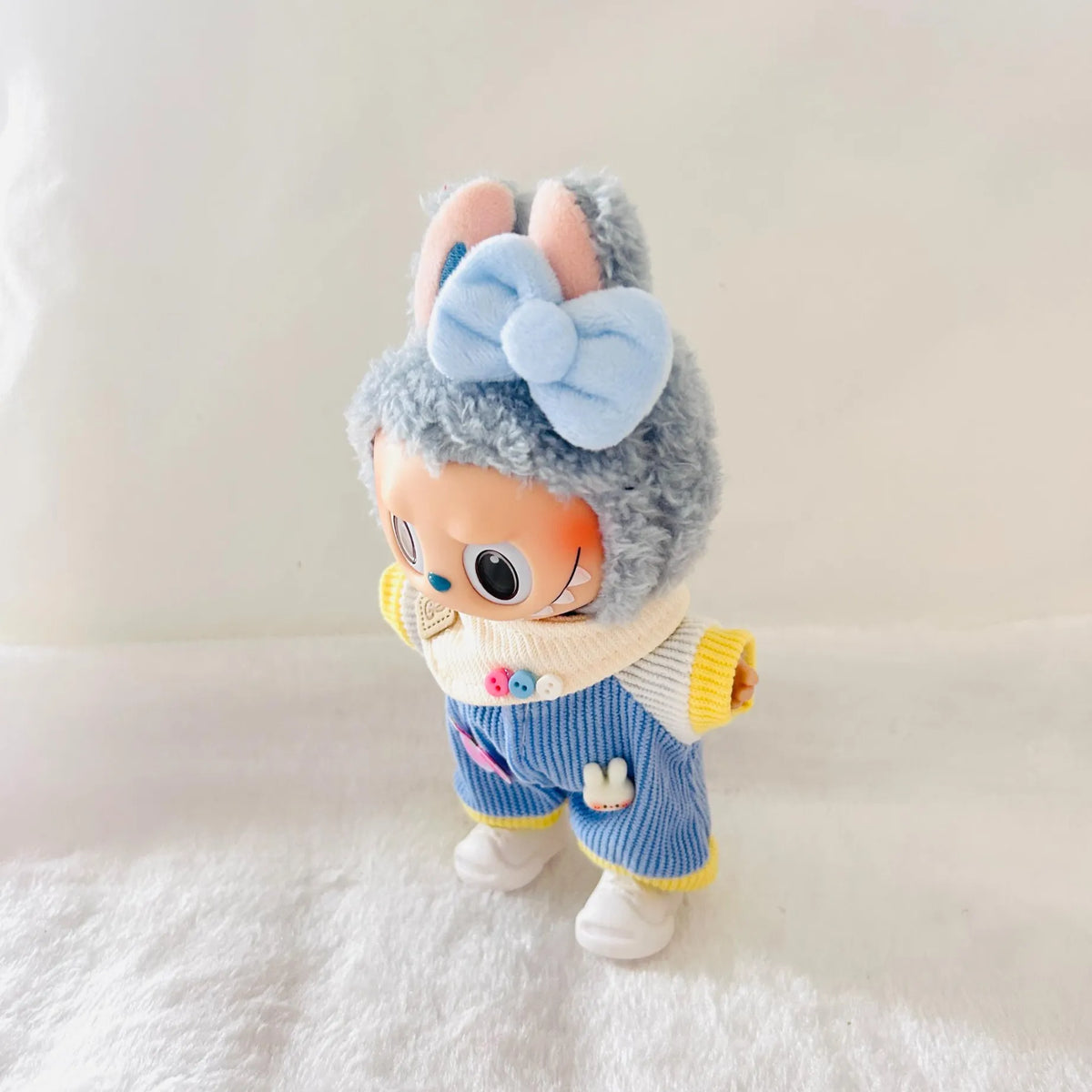 A Labubu plush doll wearing a light blue bow, and a blue striped outfit with yellow trim.
