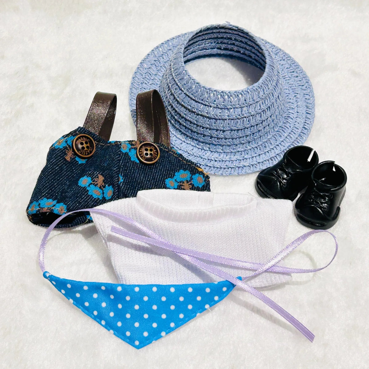 A doll outfit set including a light blue woven sun hat, a dark blue floral petticoat, a white knit top, a blue polka dot bandana, and black doll shoes.