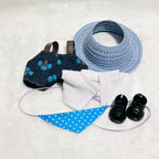 A back view of doll outfit set including a blue straw sun hat, a dark denim-style vest with blue floral print, a white shirt, a bib, and a pair of black booties.