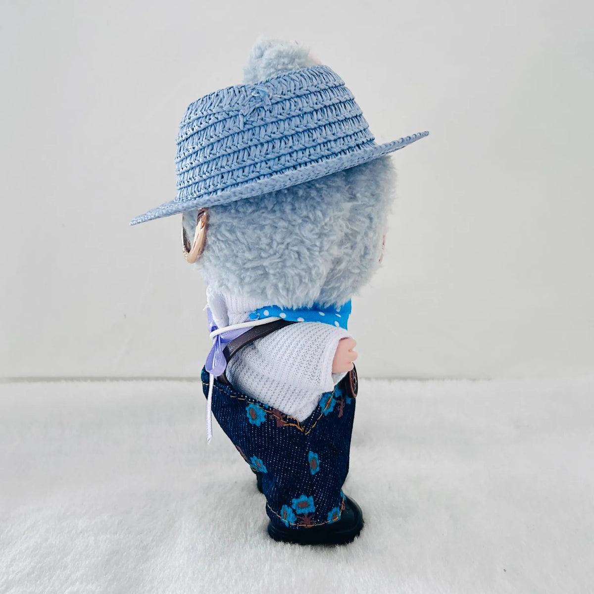 A plush doll wearing a light blue woven hat, a white knit top, and dark blue floral pants.