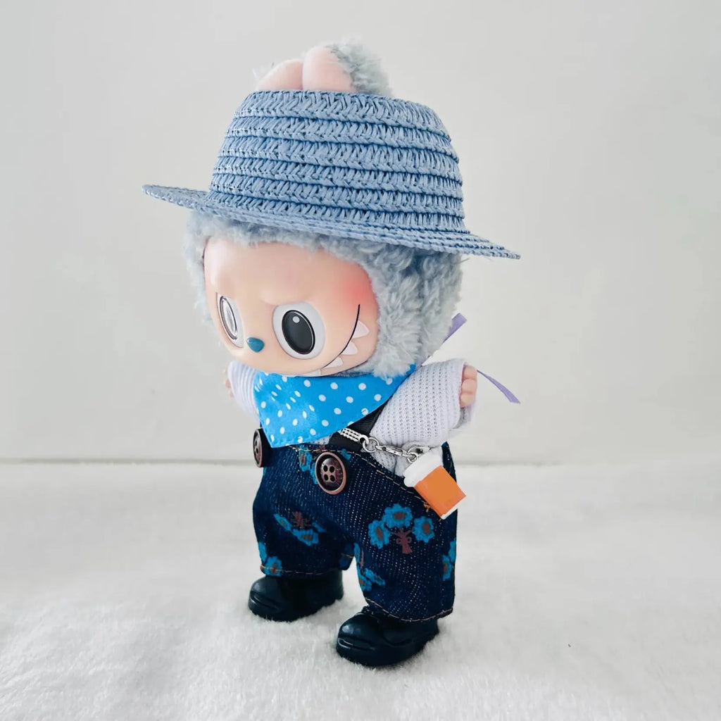 A stylized Labubu plush doll has a blue woven hat, a blue polka-dot bandana, dark blue patterned pants, and black shoes.