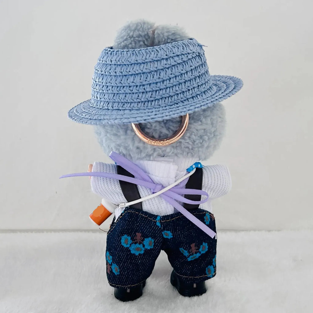 A plush toy dressed in a light blue woven hat, white shirt, black suspenders, and dark blue floral overalls.