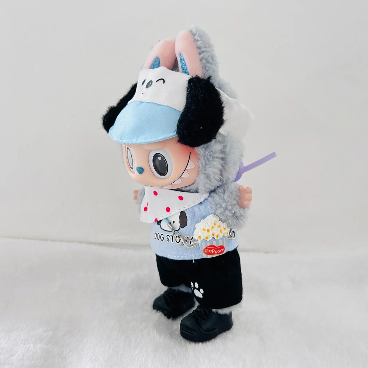 A plush toy dog dressed in a light blue visor, white bib with red polka dots, black pants, and black shoes.
