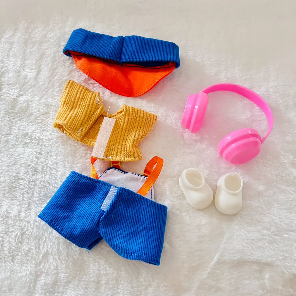 A doll clothing and accessory set including a blue and orange visor, a yellow ribbed top, blue shorts, pink headphones, and white booties.