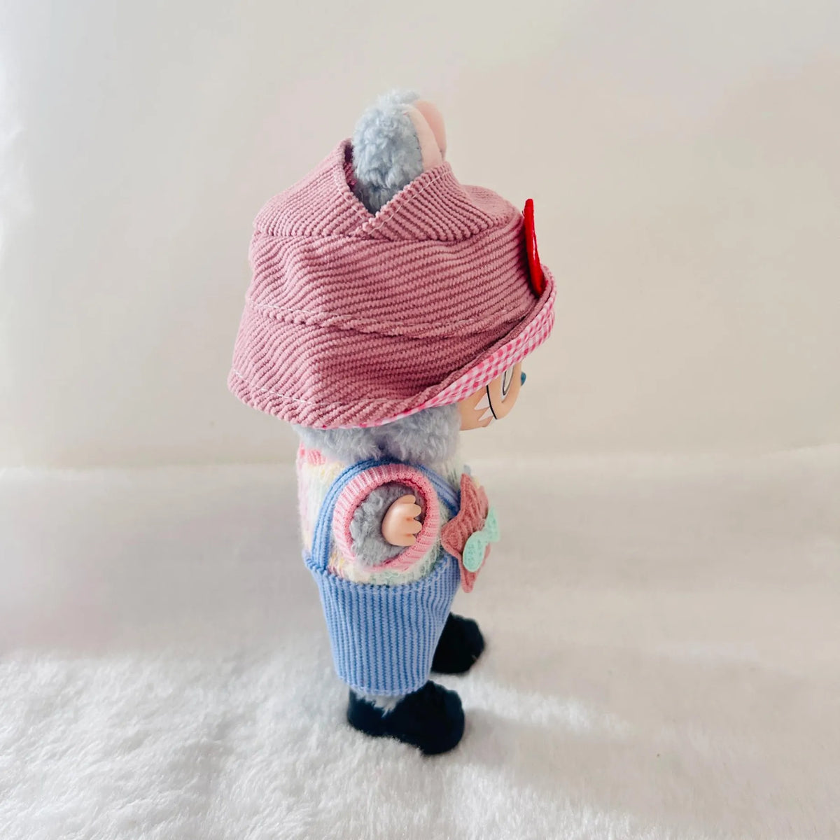 A Labubu doll wearing a pink striped knit hat, a pink top, blue striped pants, and black shoes.