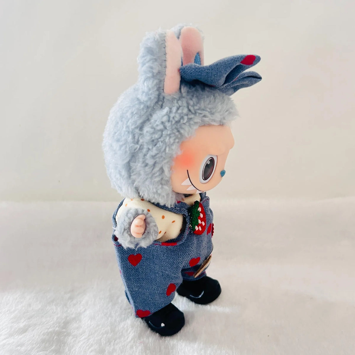 A Labubu plush doll with a denim outfit with red hearts.