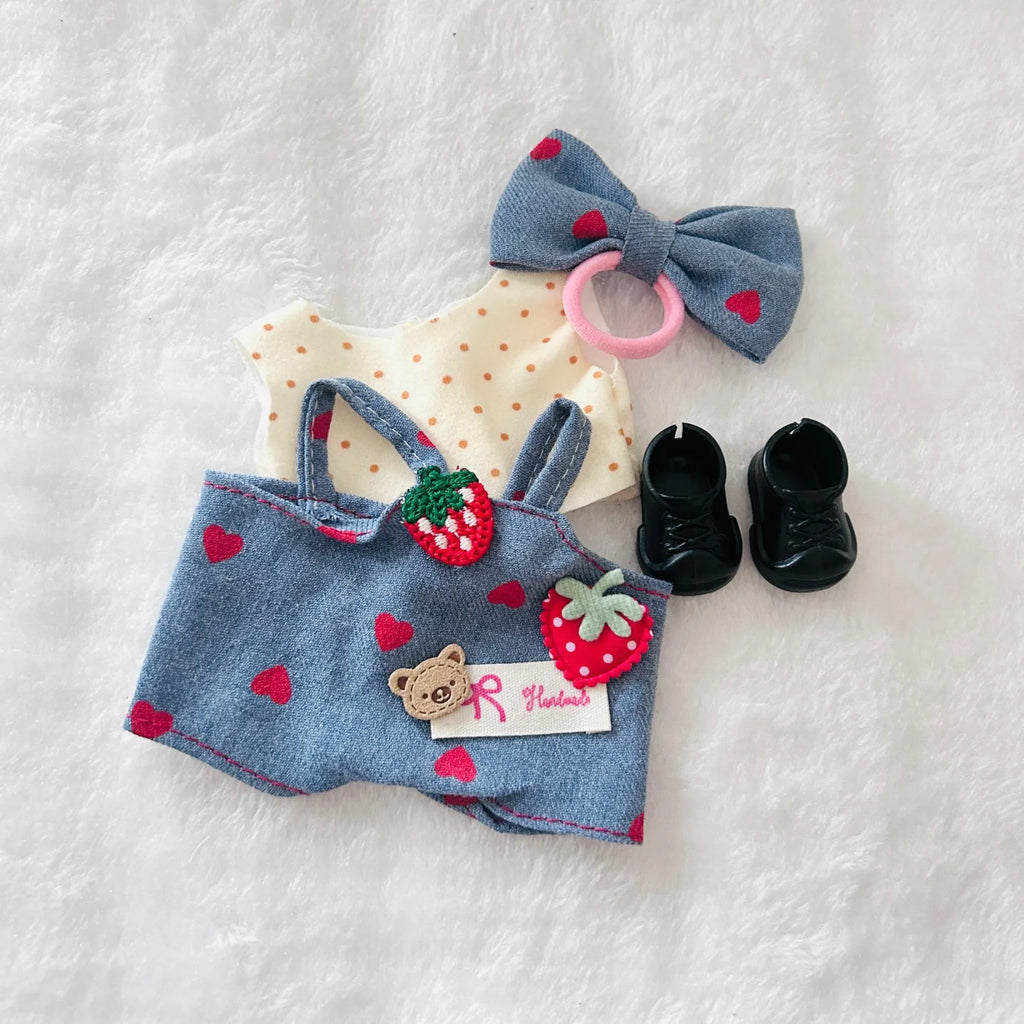 A doll outfit set including a blue denim-style romper with red heart prints and strawberry applique, a cream polka-dot top, a blue bow and a pair of black shoes.