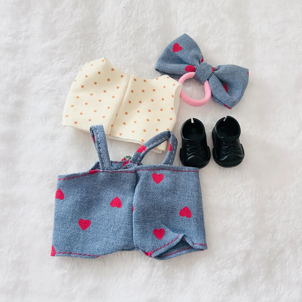 A back view of a doll outfit including a blue denim-style romper with a cream polka-dot top, a matching blue bow headband and small black booties.