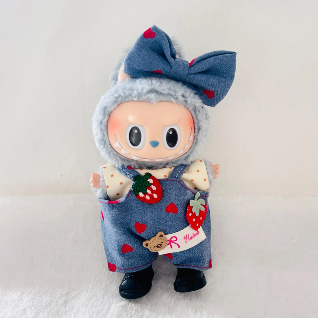 A Labubu plush doll with a blue bow decorated with red hearts. The doll is wearing blue denim-style overalls with red hearts, strawberry patches.