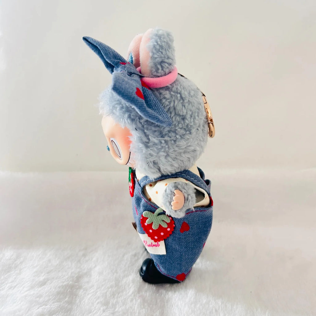 A Labubu plush doll wearing denim-style overalls with red strawberry patches.