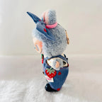A Labubu plush doll wearing denim-style overalls with red strawberry patches.