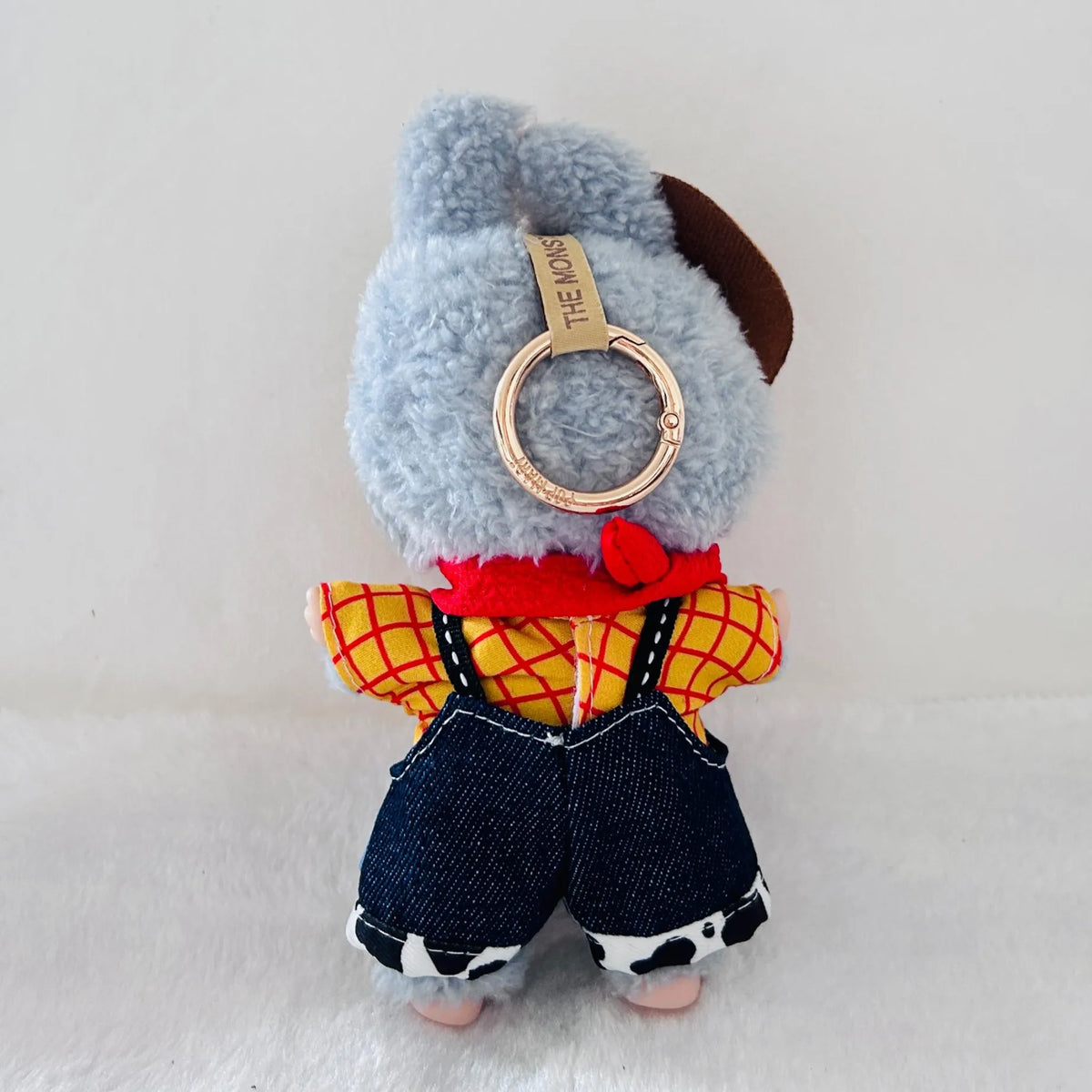 A back view of a Labubu wearing a yellow and red plaid shirt, dark blue denim overalls, and a red scarf.