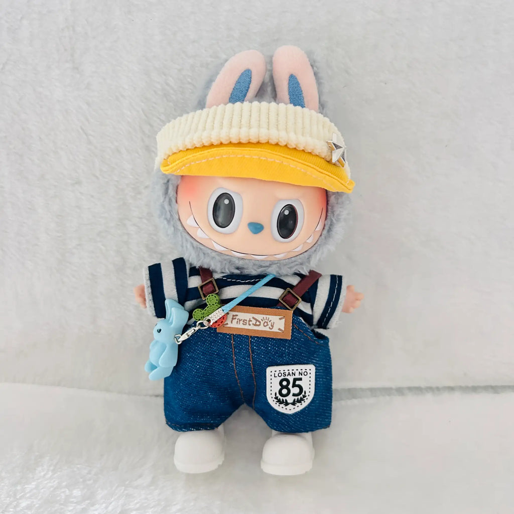 A Labubu plush doll wearing a cream ribbed cap, blue denim-style overalls with brown suspenders, a navy-and-white striped shirt, and white shoes.