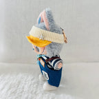 A small plush doll or character figure wearing a cream ribbed visor with a star, a yellow brim, blue denim-style overalls, and a striped shirt.