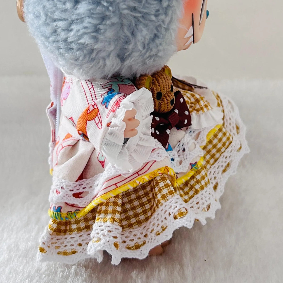 A close-up of a Labubu doll dress with yellow gingham, white lace, and a brown bear icon.