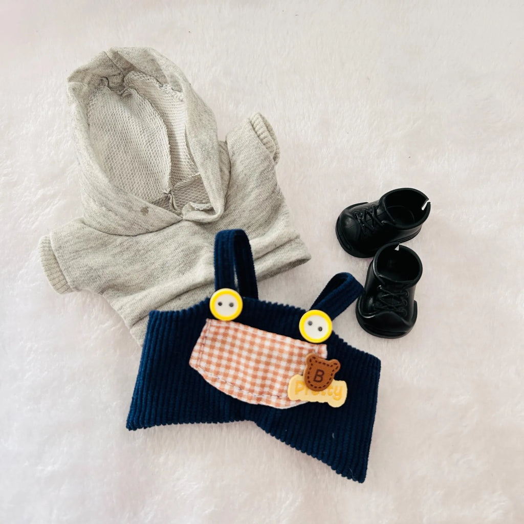 A styled flat-lay of a Labubu doll outfit set, including a light grey knit hoodie, navy blue corduroy bib, and black lace-up booties.