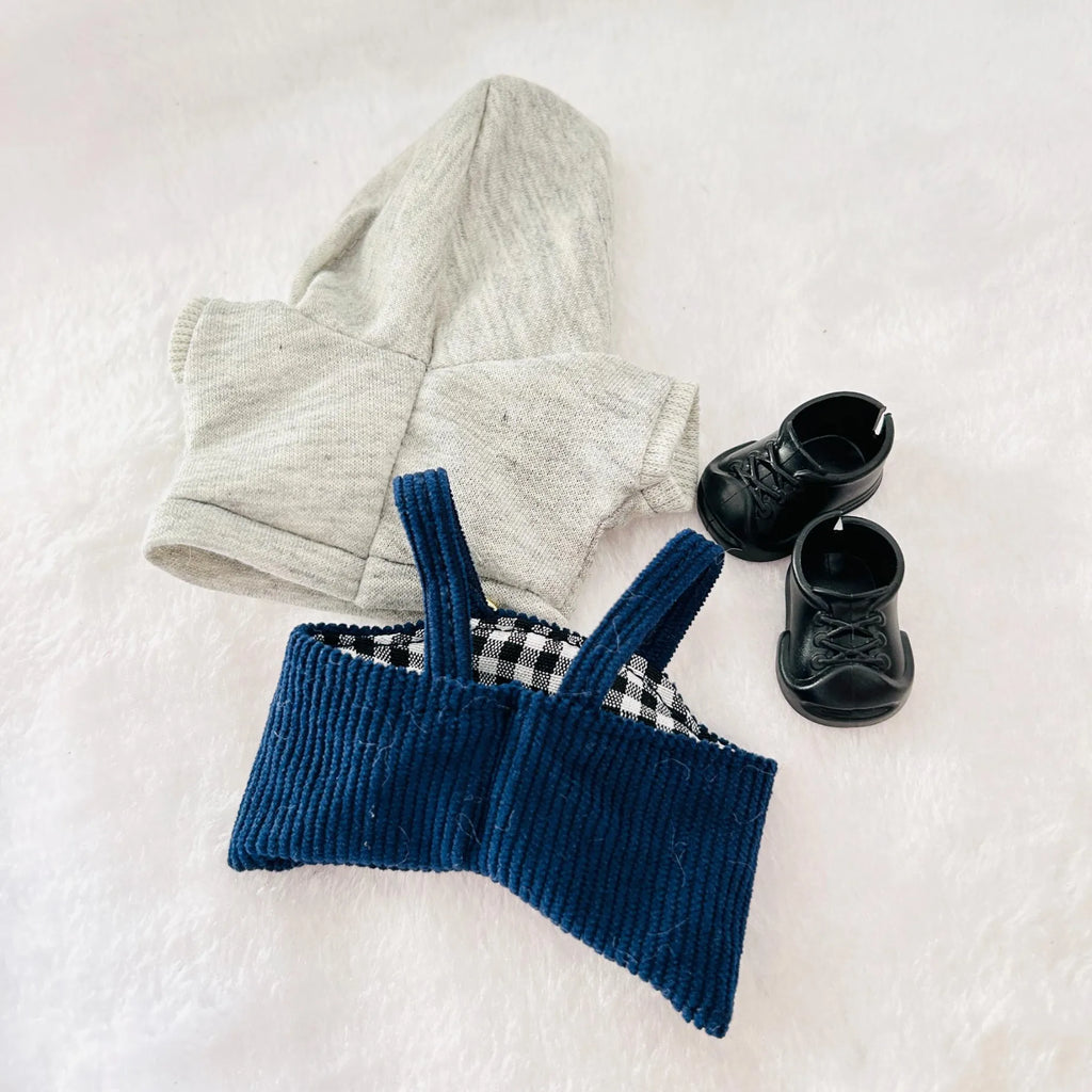 A styled flat-lay of a two-piece knit outfit for a Labubu doll, featuring a light grey  hoodie and a navy blue corduroy overall and black booties.