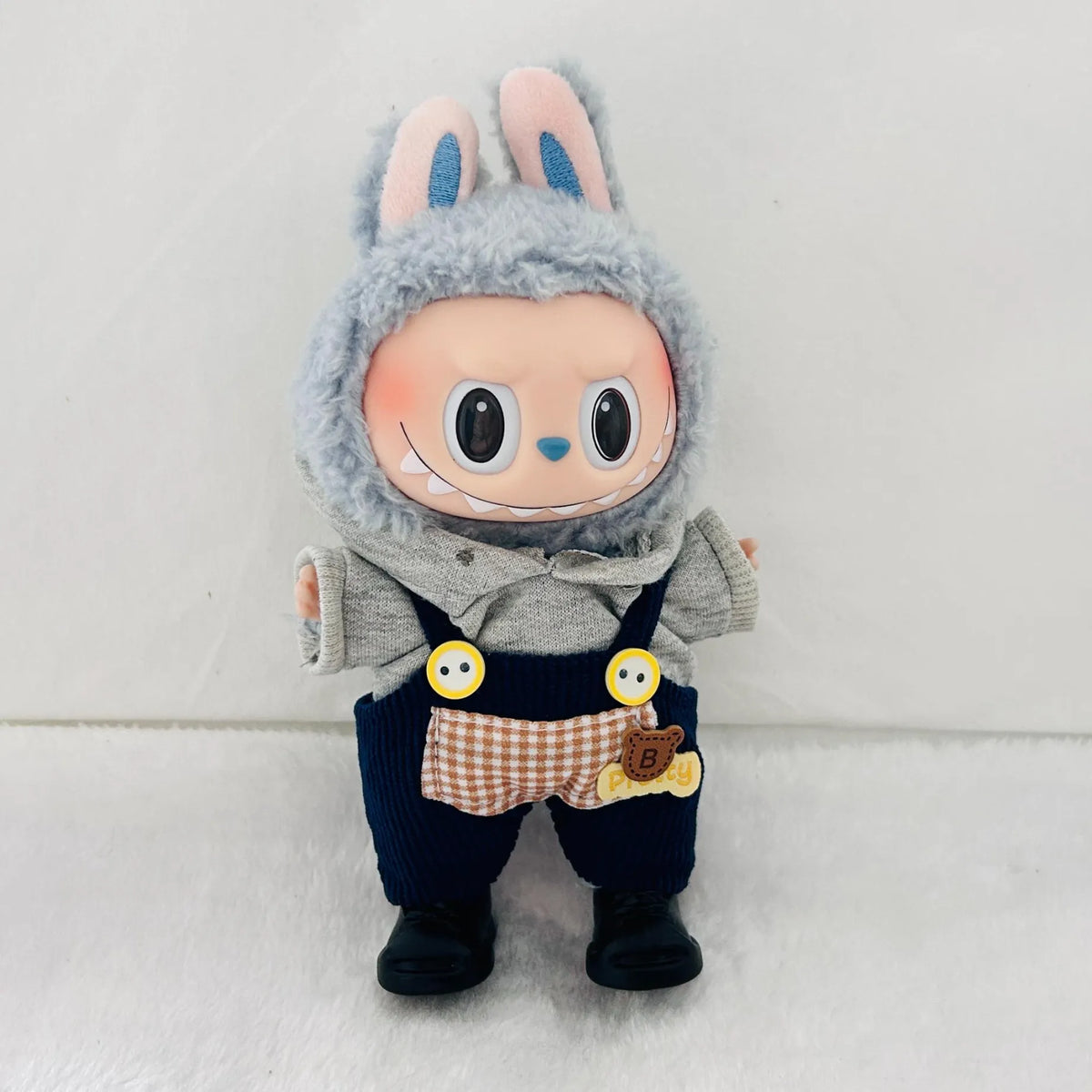 A  Labubu doll wearing a outfit set, including a light grey knit hoodie, navy blue corduroy overall, and black lace-up booties.