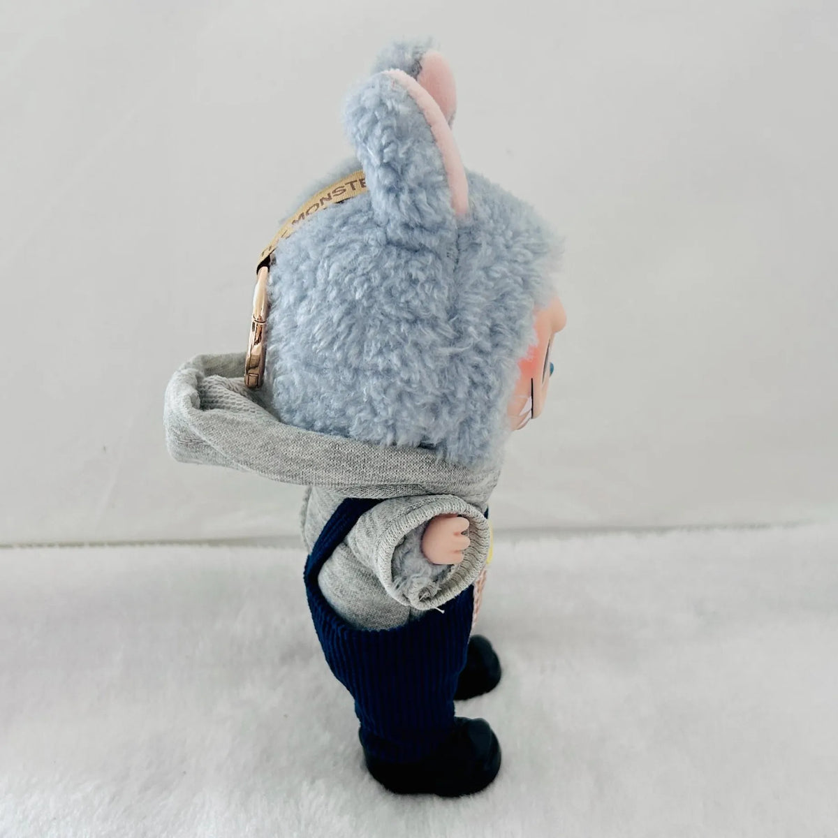 A Labubu doll with a grey hood, navy overalls, and black shoes, standing against a plain light background.