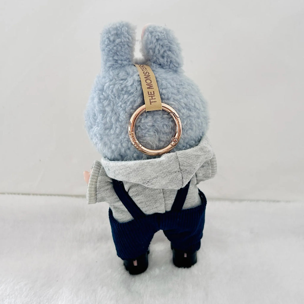 A back view a Labubu plush  doll wearing a grey hooded sweatshirt, navy blue overalls, and black shoes.