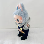 A Labubu plush doll  wearing a grey hoodie, and dark blue overalls, standing on a white textured surface.