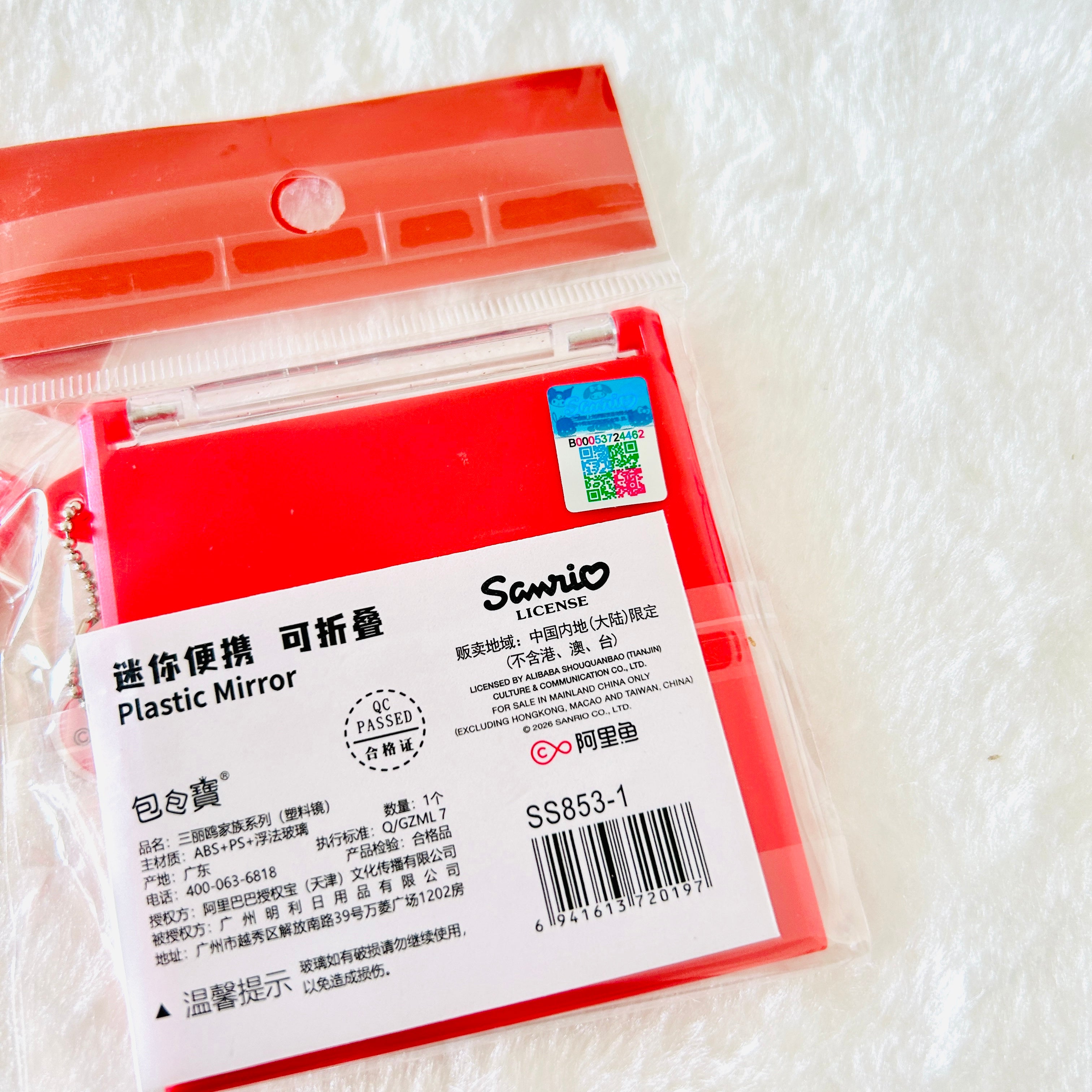 A red plastic folding mirror in its original packaging, featuring Chinese and English text, a barcode, the Sanrio brand logo on the white label, and a holographic sticker. 
