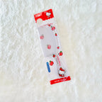 A strawberry-themed Hello Kitty hair comb in its original retail packaging, placed on a white textured faux fur surface.
