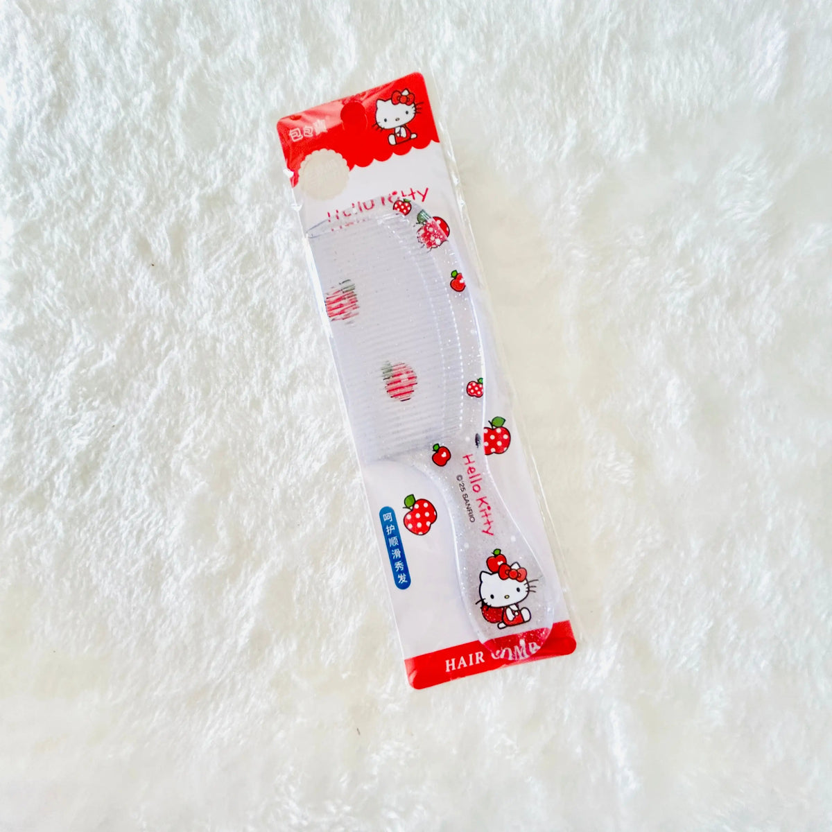 A strawberry-themed Hello Kitty hair comb in its original retail packaging, placed on a white textured faux fur surface.