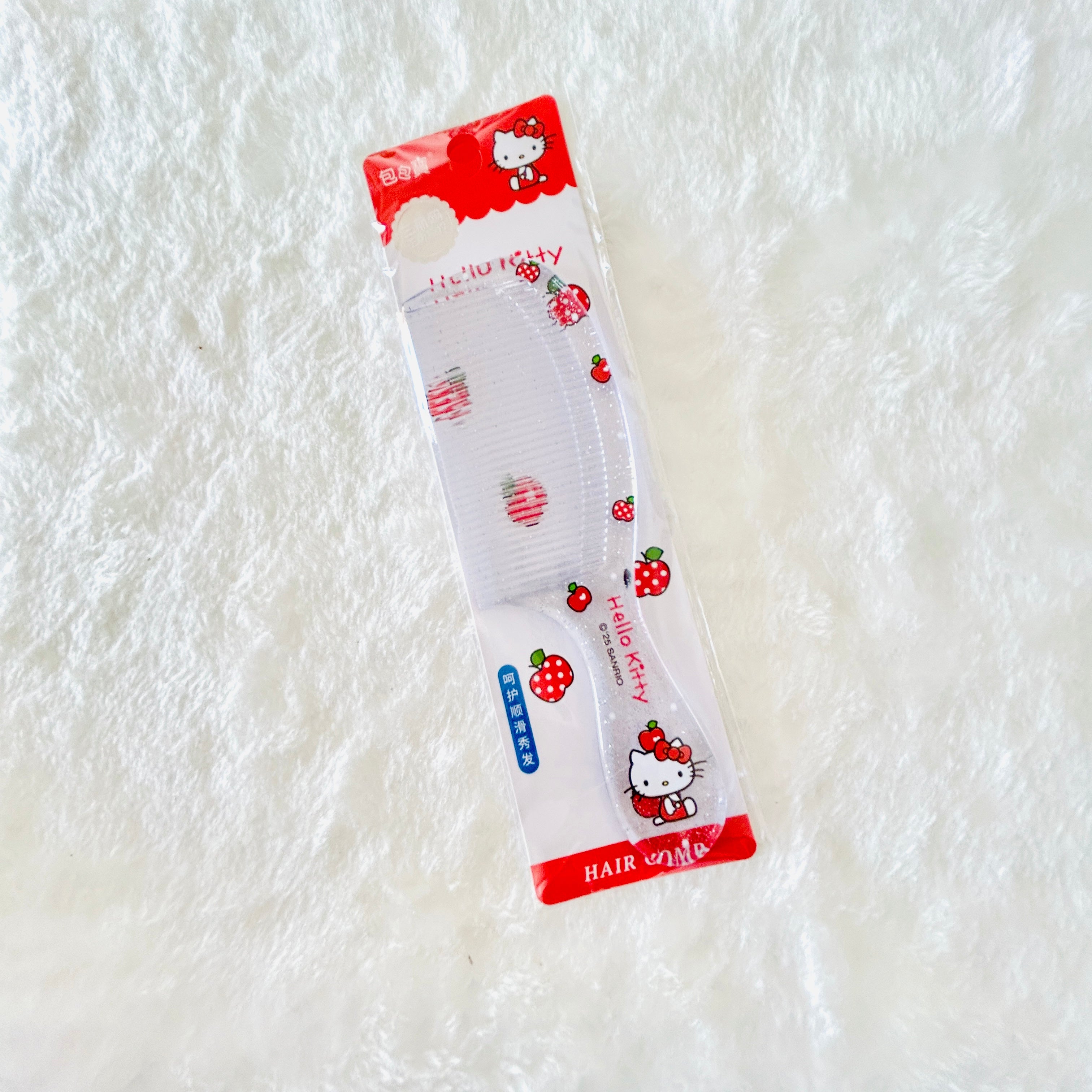 A strawberry-themed Hello Kitty hair comb in its original retail packaging, placed on a white textured faux fur surface.