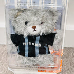 A small gray plush teddy bear inside a clear plastic display box, wearing a black and light blue striped shirt with the word 'HIRONO' printed across the front.