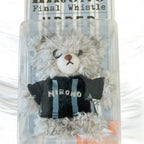 A small gray plush teddy bear with a white snout and black embroidered eyes, wearing a black and blue striped shirt with the word 'HIRONO' on the front, displayed inside a clear plastic box.