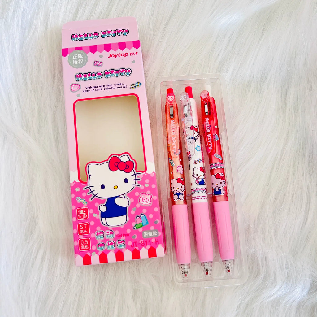 Hello Kitty themed stationery set featuring a pink branded box and three cartoon-print retractable pens in a clear plastic case, placed on a white faux-fur surface.