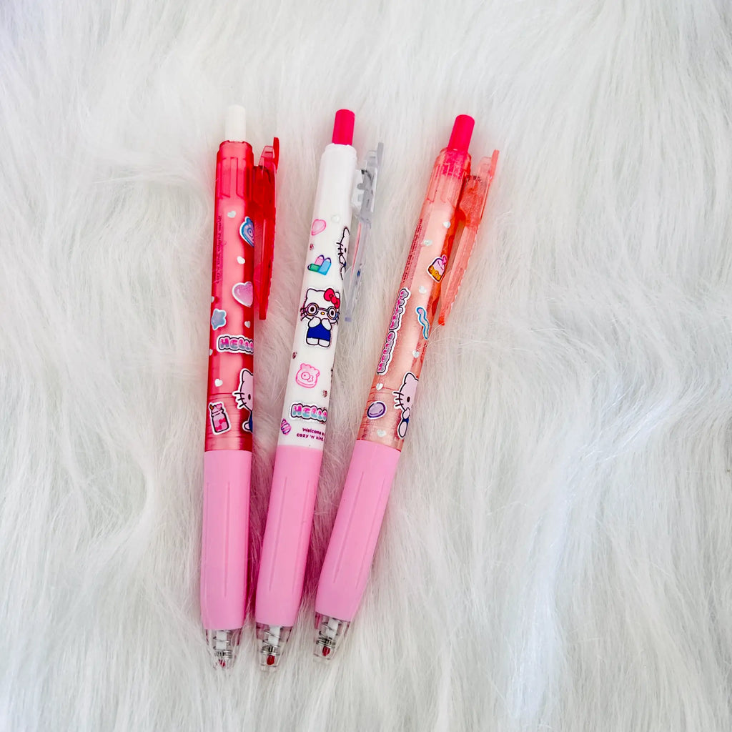 Three cartoon-themed retractable gel pens in pink, red, and white, decorated with Hello Kitty and Sanrio character illustrations, arranged on a white faux fur background.