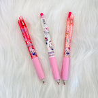 Three Hello Kitty retractable mechanical pencils in red, clear, and pink, arranged diagonally on a white faux fur background.