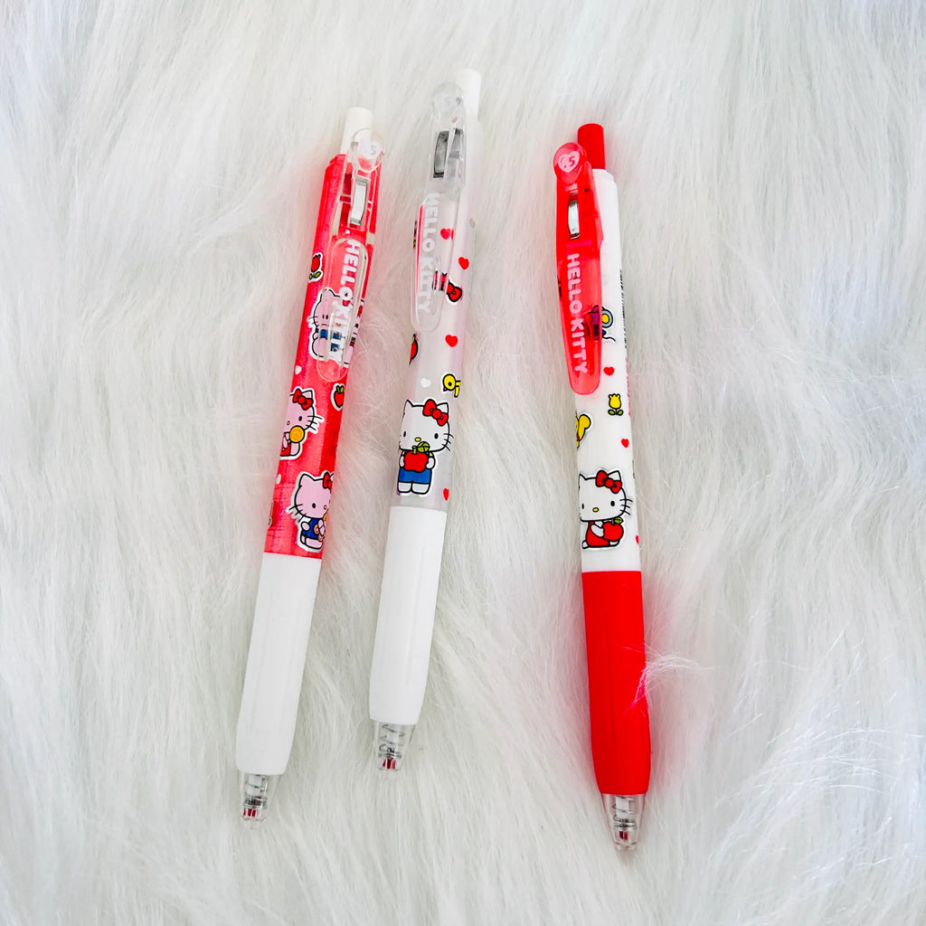 Three Hello Kitty retractable ballpoint pens in red and white cartoon-themed designs, arranged vertically on a white faux fur background.