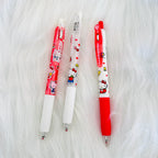 Three Hello Kitty retractable ballpoint pens in red and white cartoon-themed designs, arranged vertically on a white faux fur background.