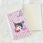 Kuromi A5 lined notebook with a pastel purple and white checkered cover featuring Kuromi and a purple cloud character, shown with an open notebook on a white textured background.