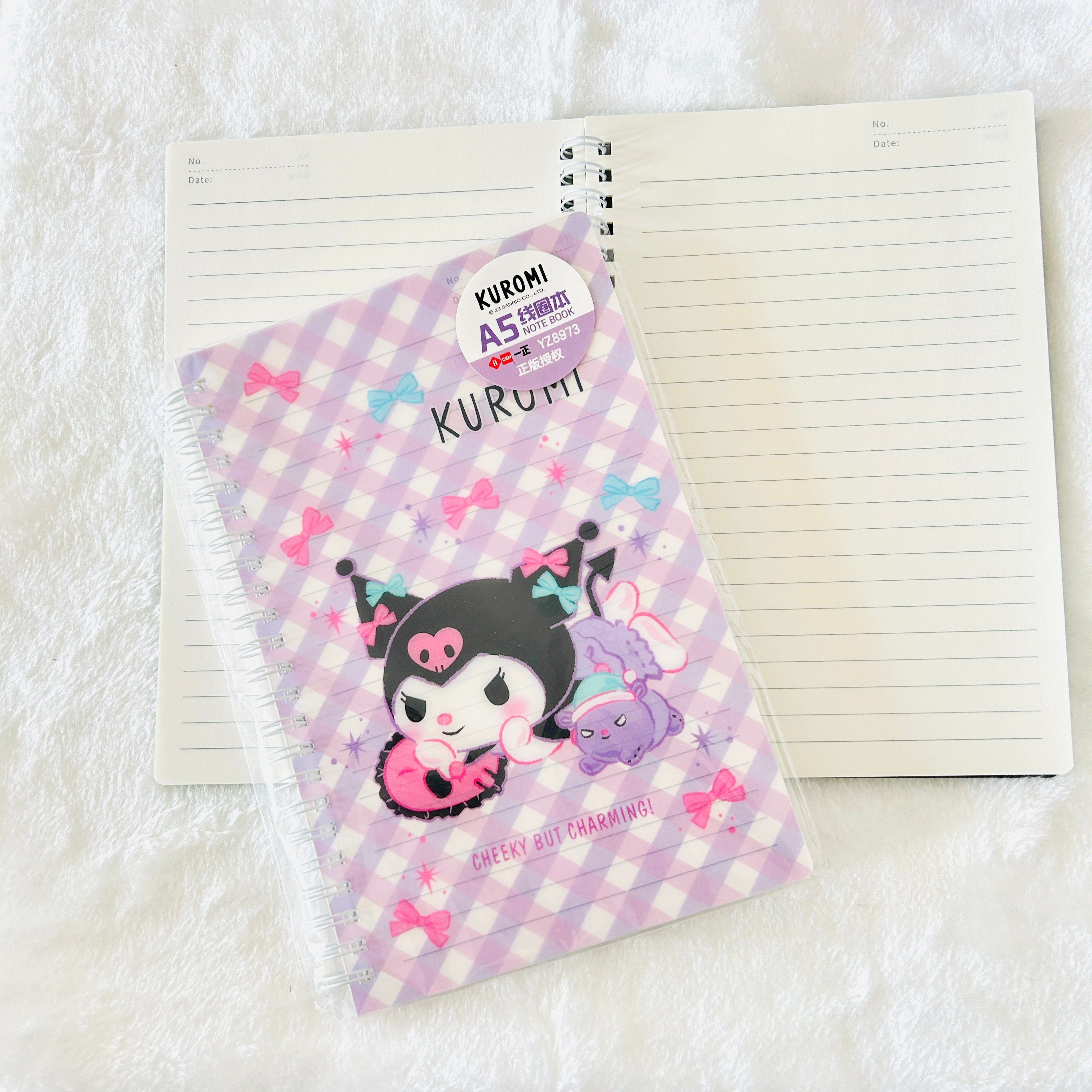 Kuromi A5 lined notebook with a pastel purple and white checkered cover featuring Kuromi and a purple cloud character, shown with an open notebook on a white textured background.