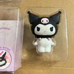 Kuromi character novelty item in clear plastic packaging, shown next to its branded box on a tan surface.