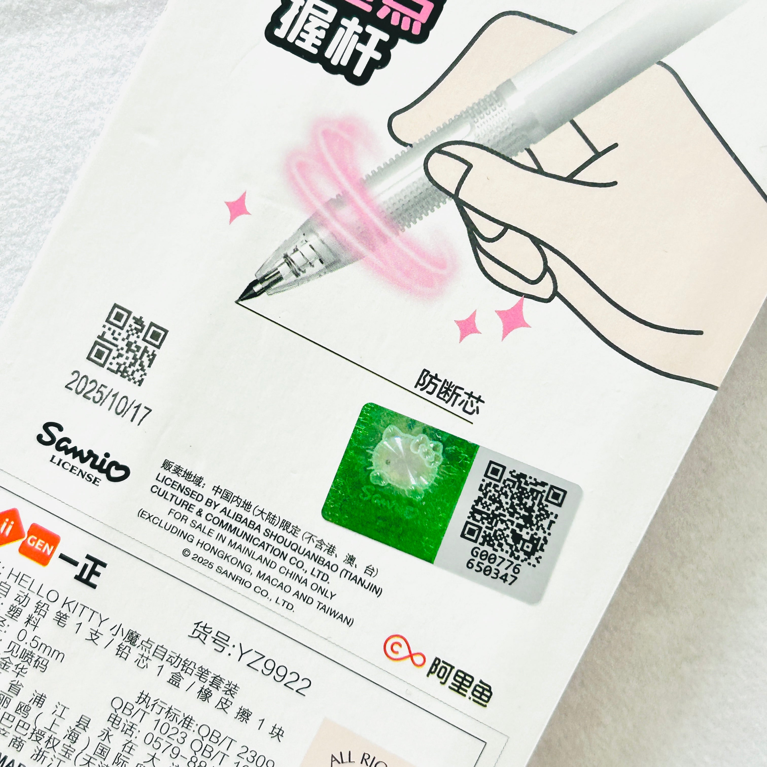 A close-up of a white Hello Kitty branded product card featuring a hand illustration holding a transparent pen with pink swirl graphics, Chinese text, QR codes, and a green Hello Kitty logo patch.