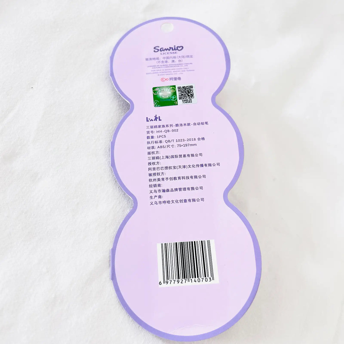 A light purple huggie-shaped product tag or packaging insert with printed text, a barcode, and a small green square graphic, photographed on a white textured fabric background.