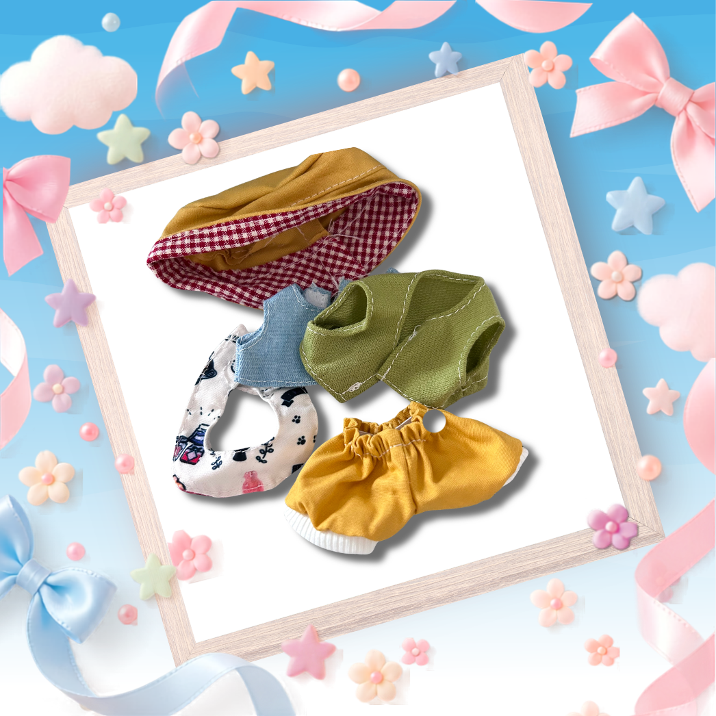 Four miniature doll clothing items arranged on a white card inside a wooden frame, surrounded by pastel decorative bows, stars, and flowers on a blue background.