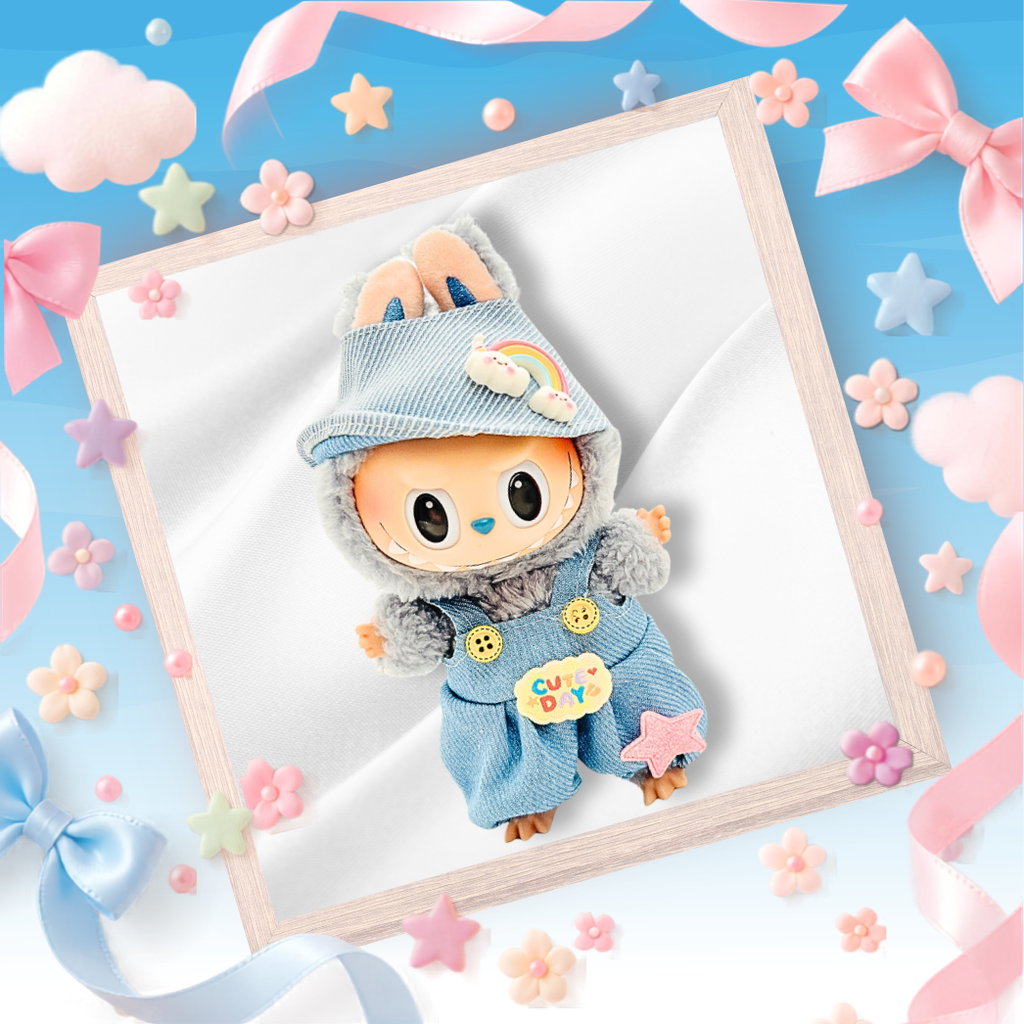 A cute plush toy doll with large black eyes, wearing a light blue denim-style outfit and matching hat with pastel rainbow and star details.