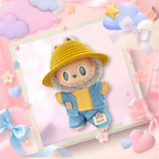 A cute plush toy character dressed in a yellow woven hat and denim overalls with a fuzzy gray hood, displayed inside a decorative white frame on a pastel pink background with bows, stars, and hearts.